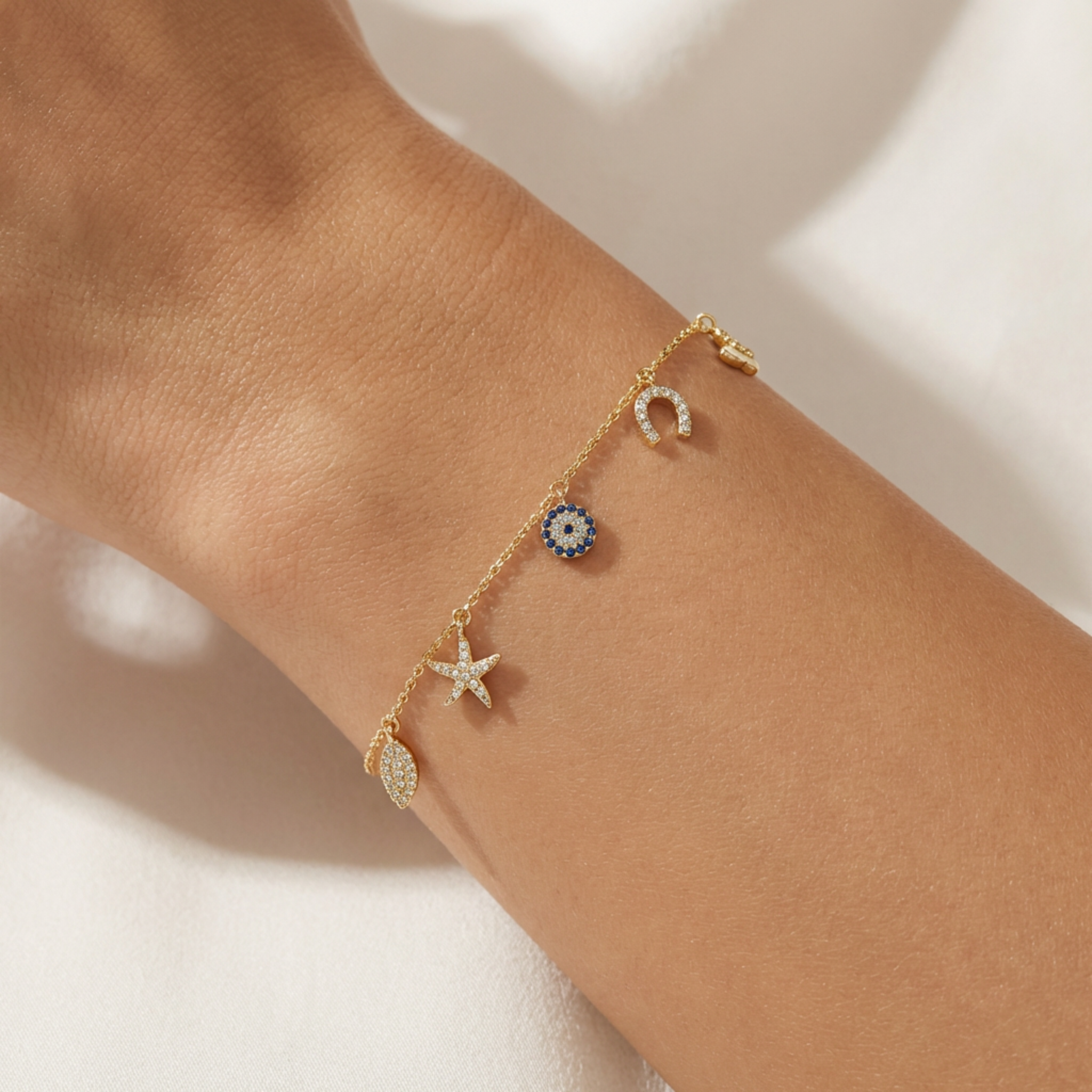 Gold bracelet with starfish, moon, and sun charms on a wrist against a neutral background
