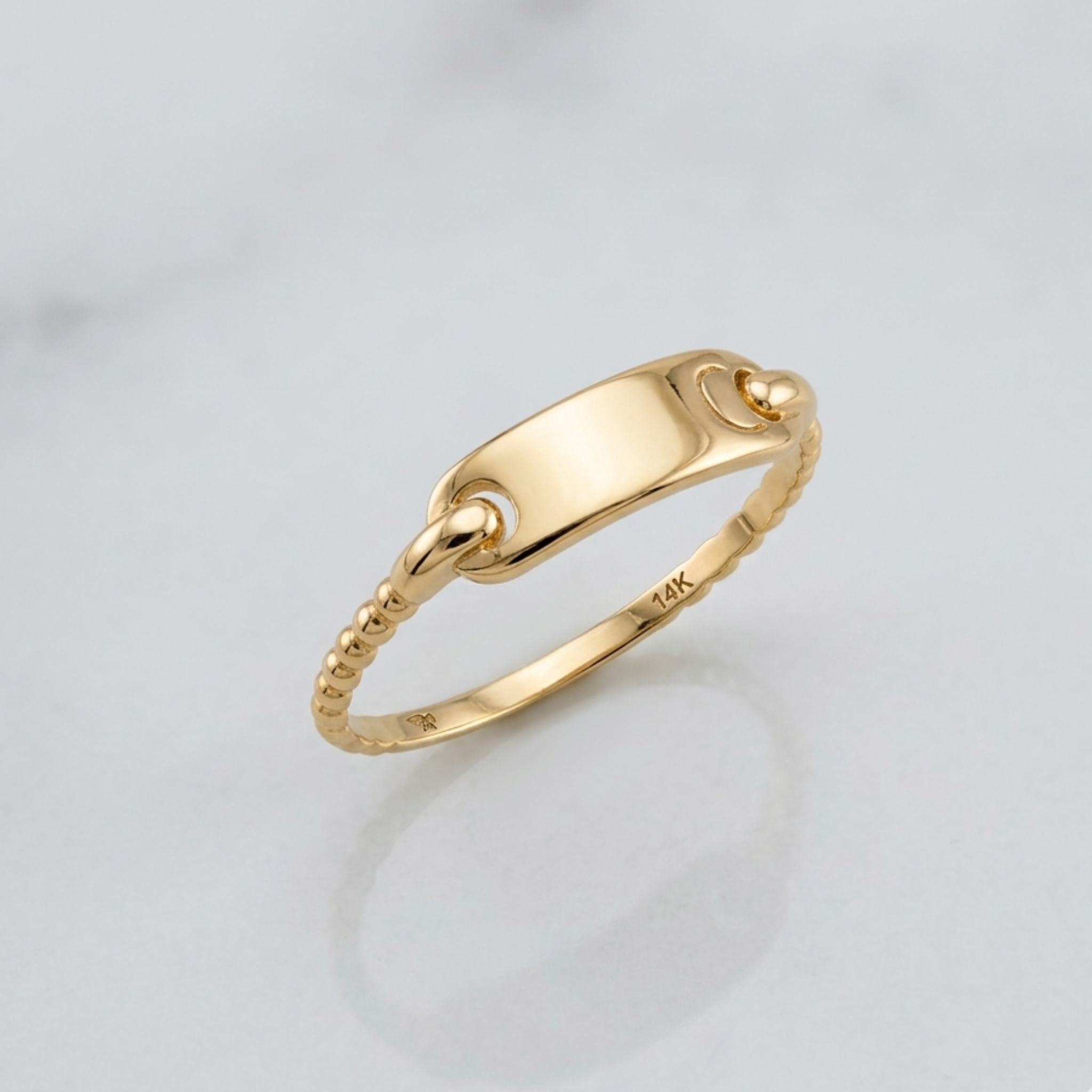 Close-up of a 14k yellow gold identity ring featuring a smooth rectangular nameplate and a curb-style chain link band, high-polish finish, jewelry photography.