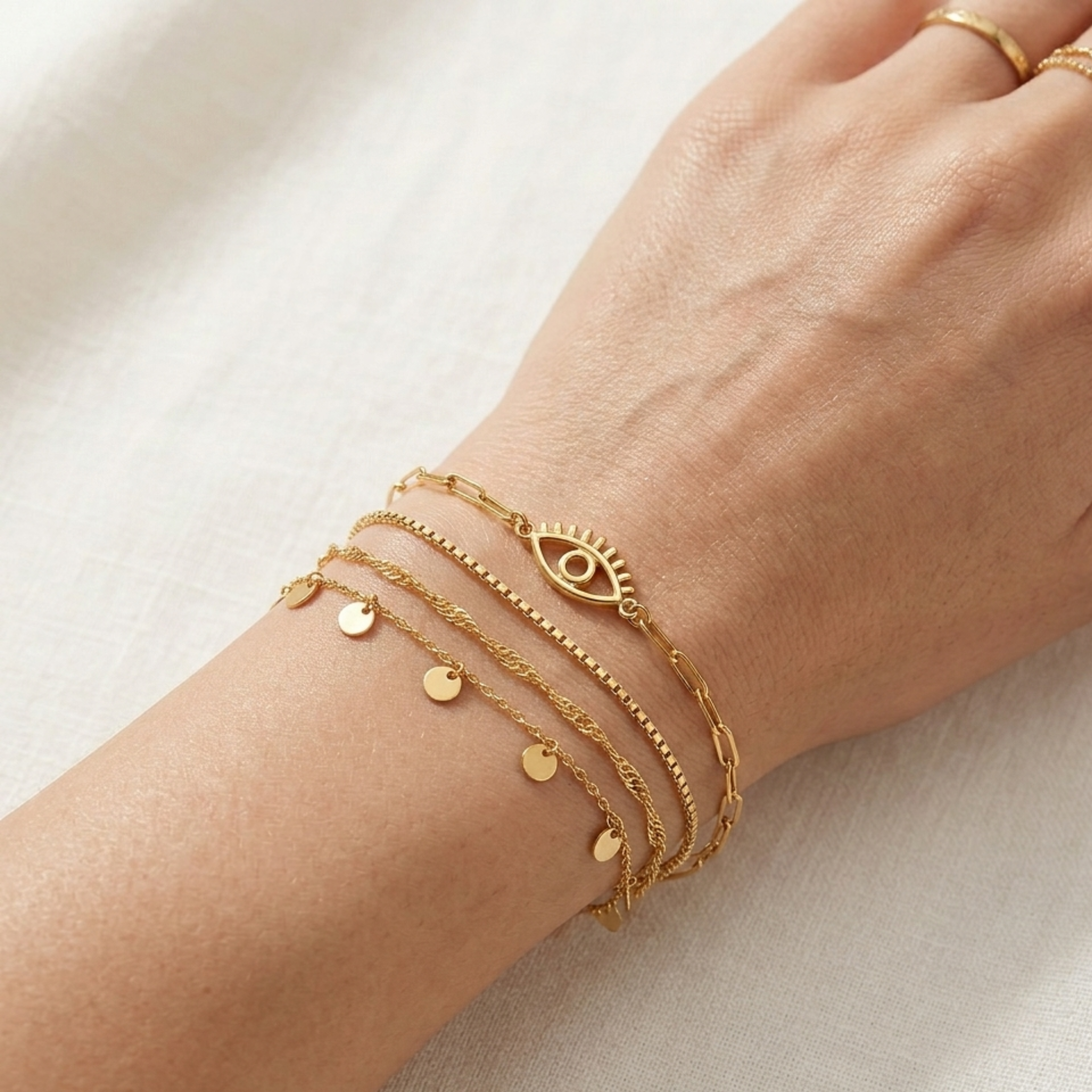 close up of gold evil eye bracelet on skin, other layer sleek dainty chain no stone centerpiece