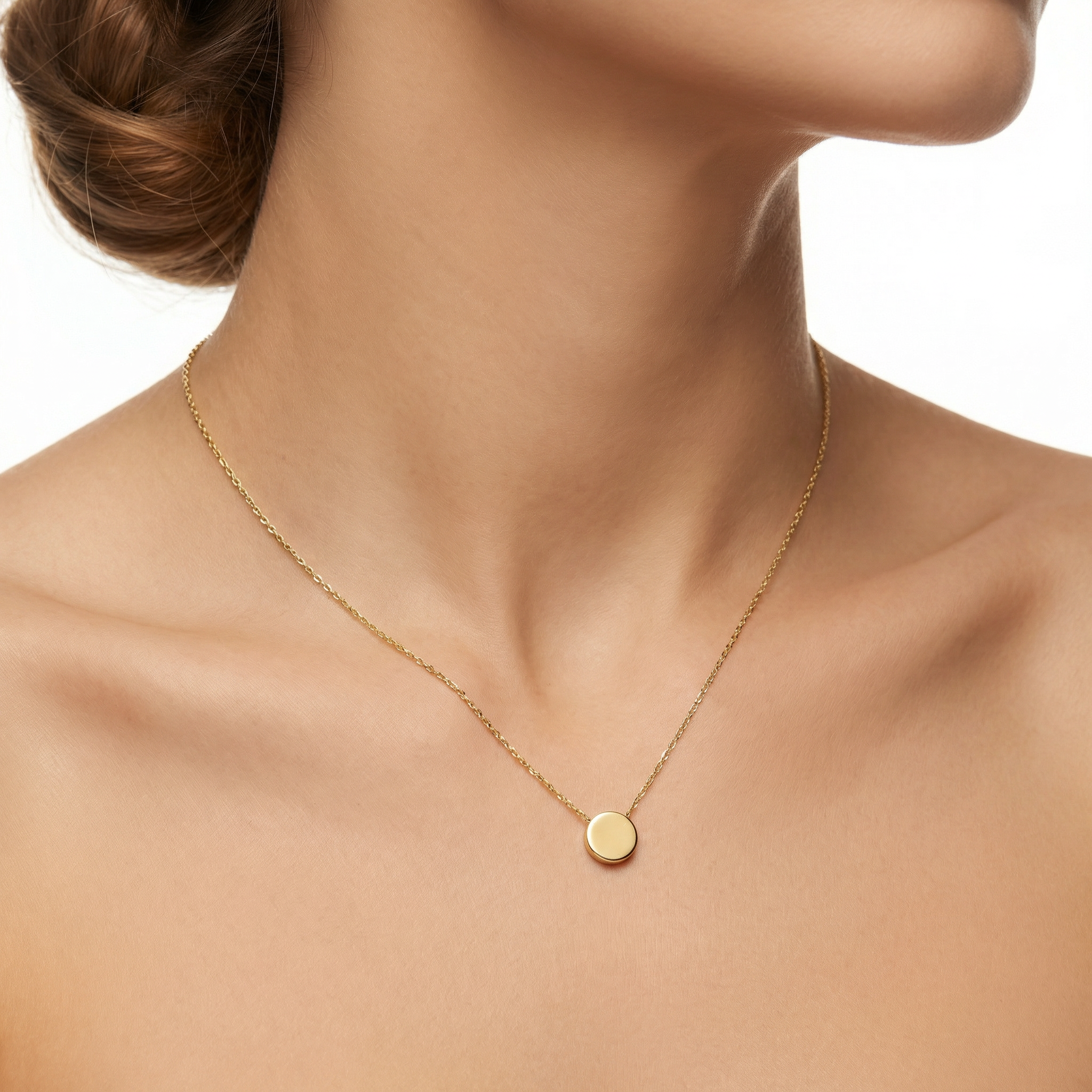 Gold necklace with a round pendant on a person's neck against a neutral background